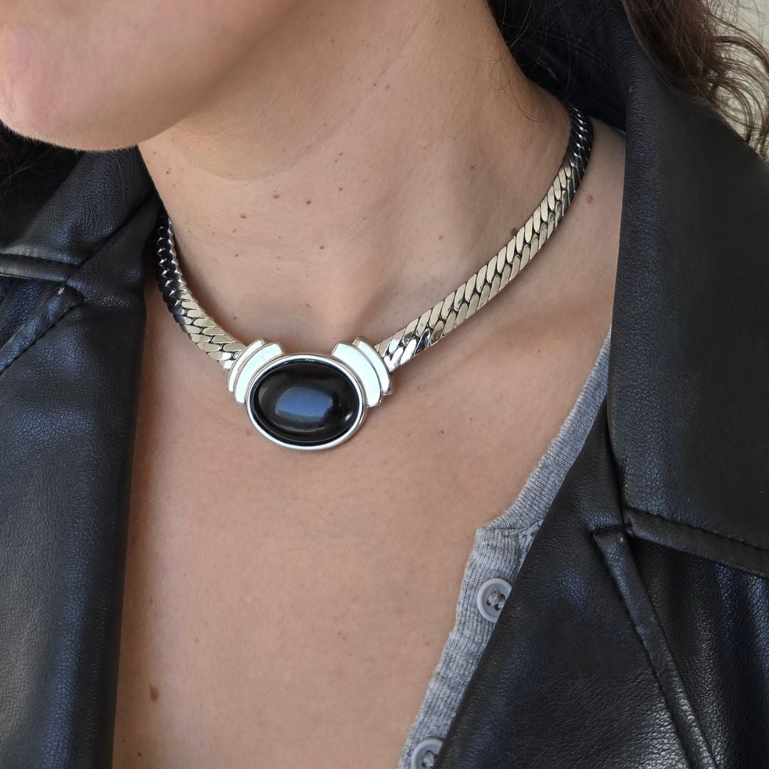 Necklace with a black stone pendant worn by a person in a leather jacket.