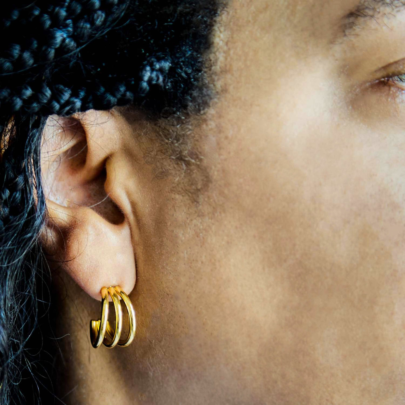Close-up of an ear wearing a gold hoop earring with hair styled in braids.