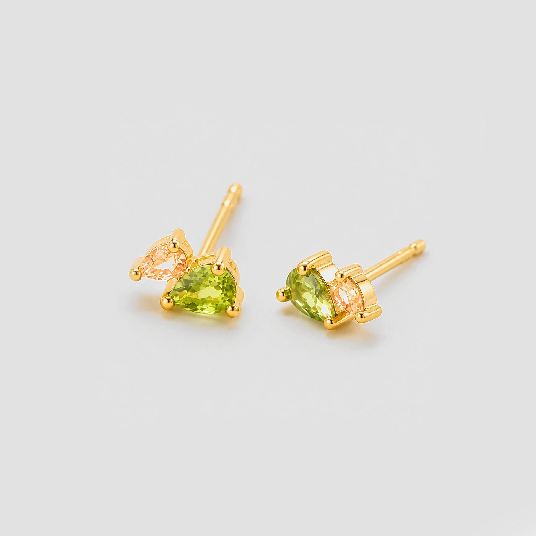 Gold earrings with green gemstones on a light gray background