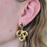 Gold Celtic knot earring worn by a person with blonde hair.