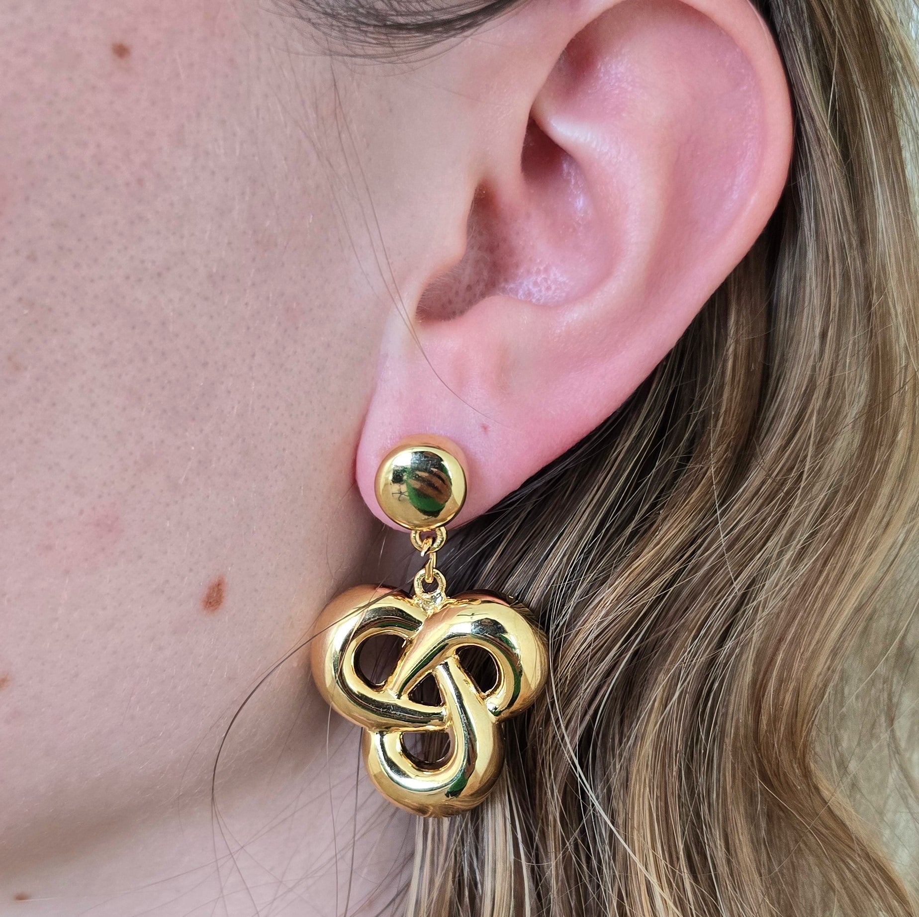 Gold Celtic knot earring worn by a person with blonde hair.