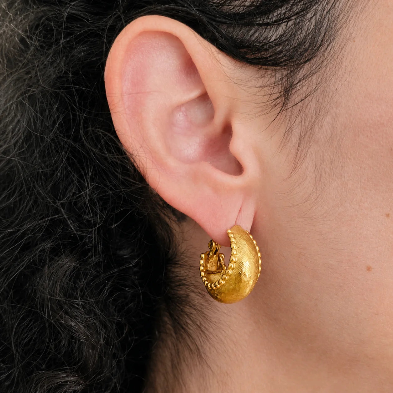 Model wearing Vintage gold-tone granulated crescent hoop earring, side view