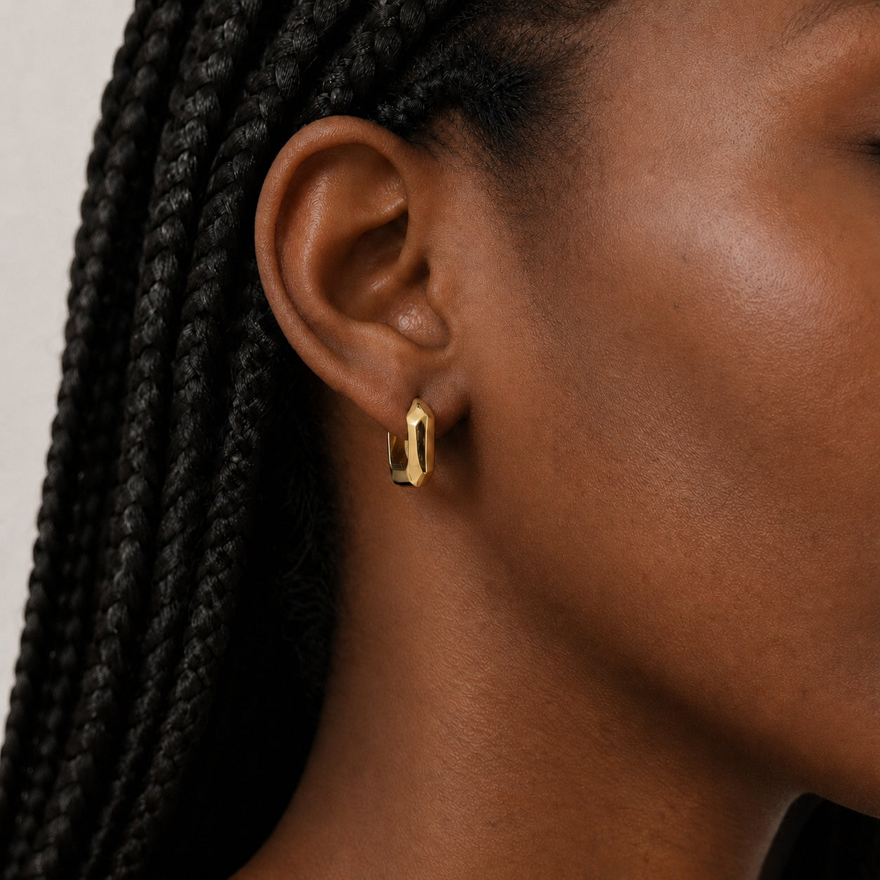 Close-up of an ear wearing a gold square hoop earring with braided hair.