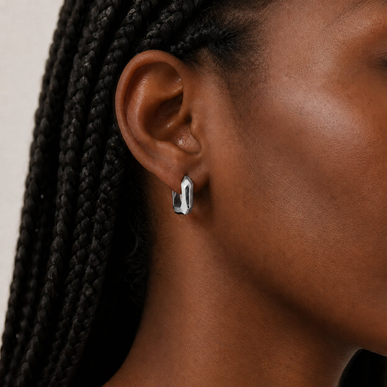Close-up of an ear wearing a silver square hoop earring with braided hair.