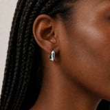 Close-up of an ear wearing a silver square hoop earring with braided hair.