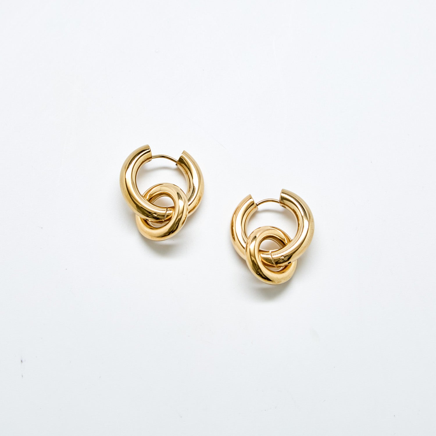 Gold interlocking hoop earrings against white background with removable charm detail in polished stainless steel, modern statement hoop design.