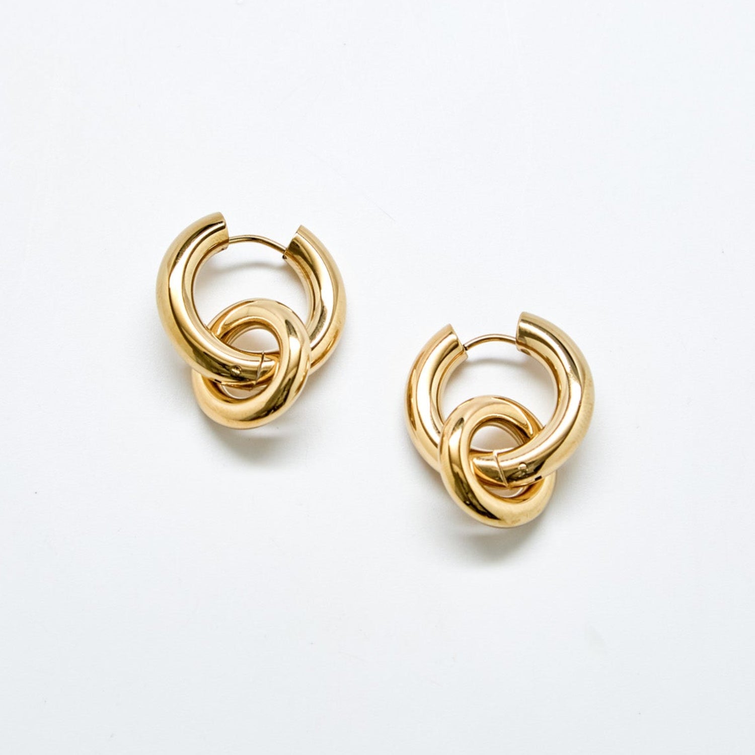 Gold interlocking hoop earrings against white background with removable charm detail in polished stainless steel, modern statement hoop design.