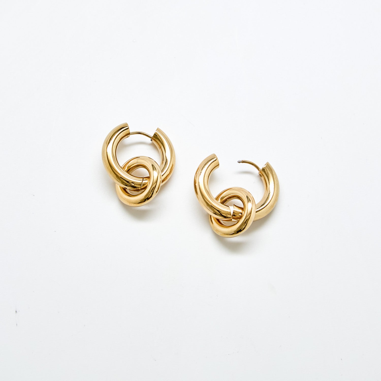Polished gold stainless steel hoop earrings against white background featuring detachable interlocking loop charm, modern sculptural jewelry design.