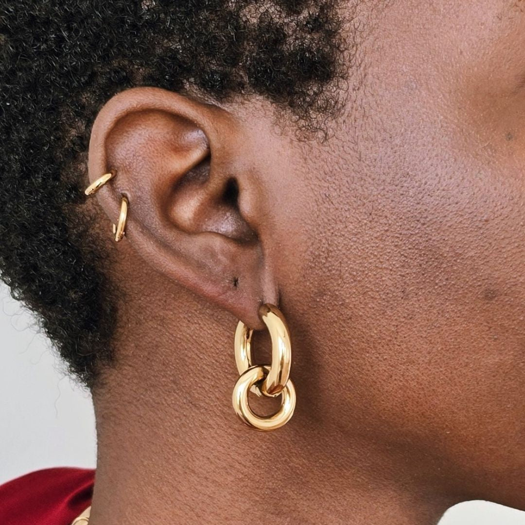 Close up of model wearing gold interlocking hoop earrings with removable charm, chunky gold statement hoop earrings in polished stainless steel.
