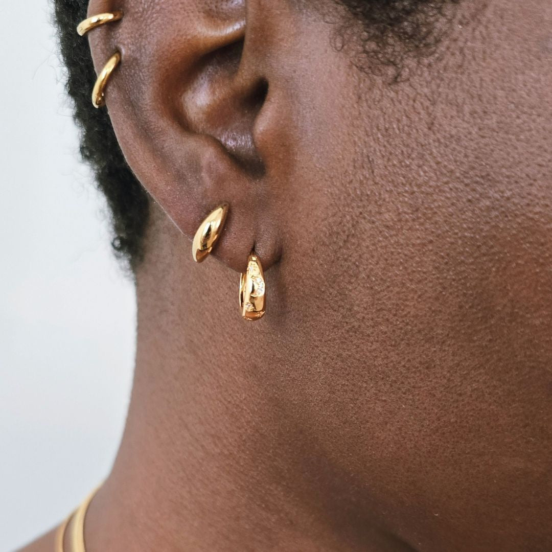 Close-up of ear wearing small curved gold stud earrings paired with medium gold hoop earrings.