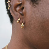 Close-up of ear wearing small curved gold stud earrings paired with medium gold hoop earrings.