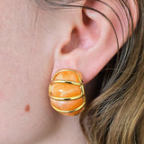 Close-up of an ear wearing a gold and orange earring.
