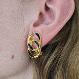 Gold and black earring worn by a person with brown hair.