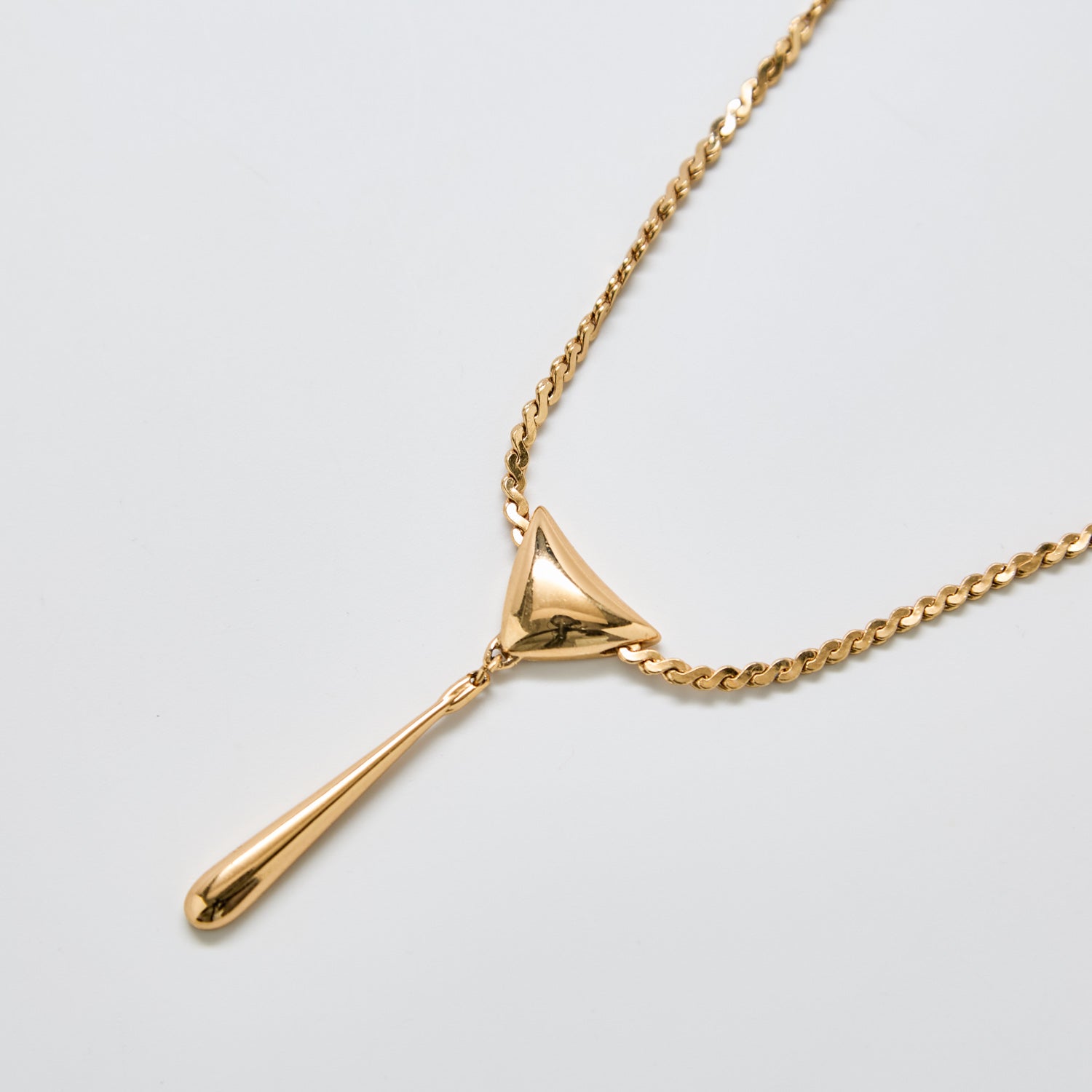 Close-up of vintage Monet gold modernist necklace featuring a geometric triangle and elongated teardrop pendant on a polished gold chain.
