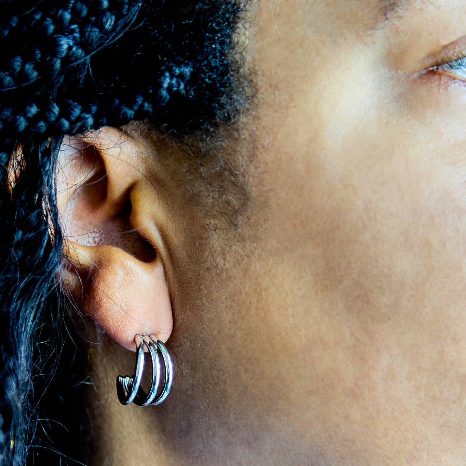 Close-up of an ear with a silver earring, hair styled in braids.