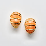 Pair of earrings with orange stone and gold accents on a light gray background
