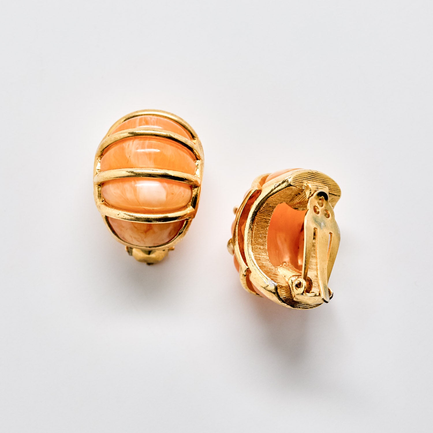 Gold earrings with peach-colored stones on a light gray background