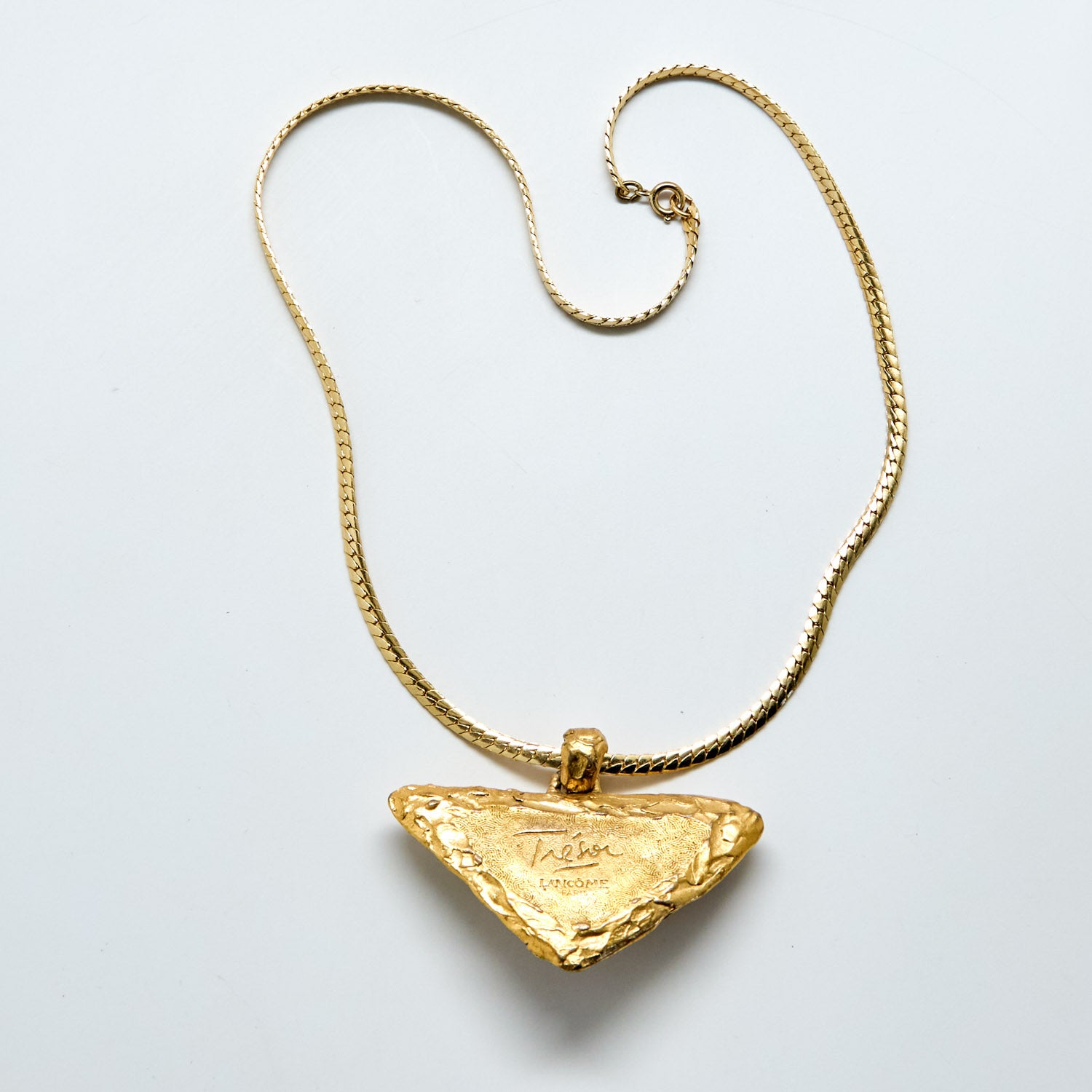 Gold necklace with a triangular pendant on a light gray background