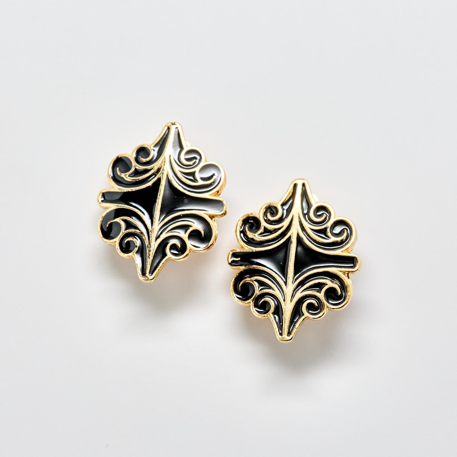Pair of black and gold decorative earrings on a light gray background