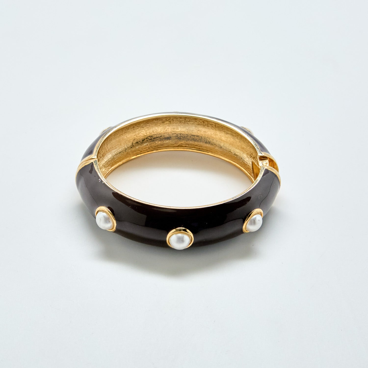 Black and gold bracelet with pearl-like stones on a light gray background