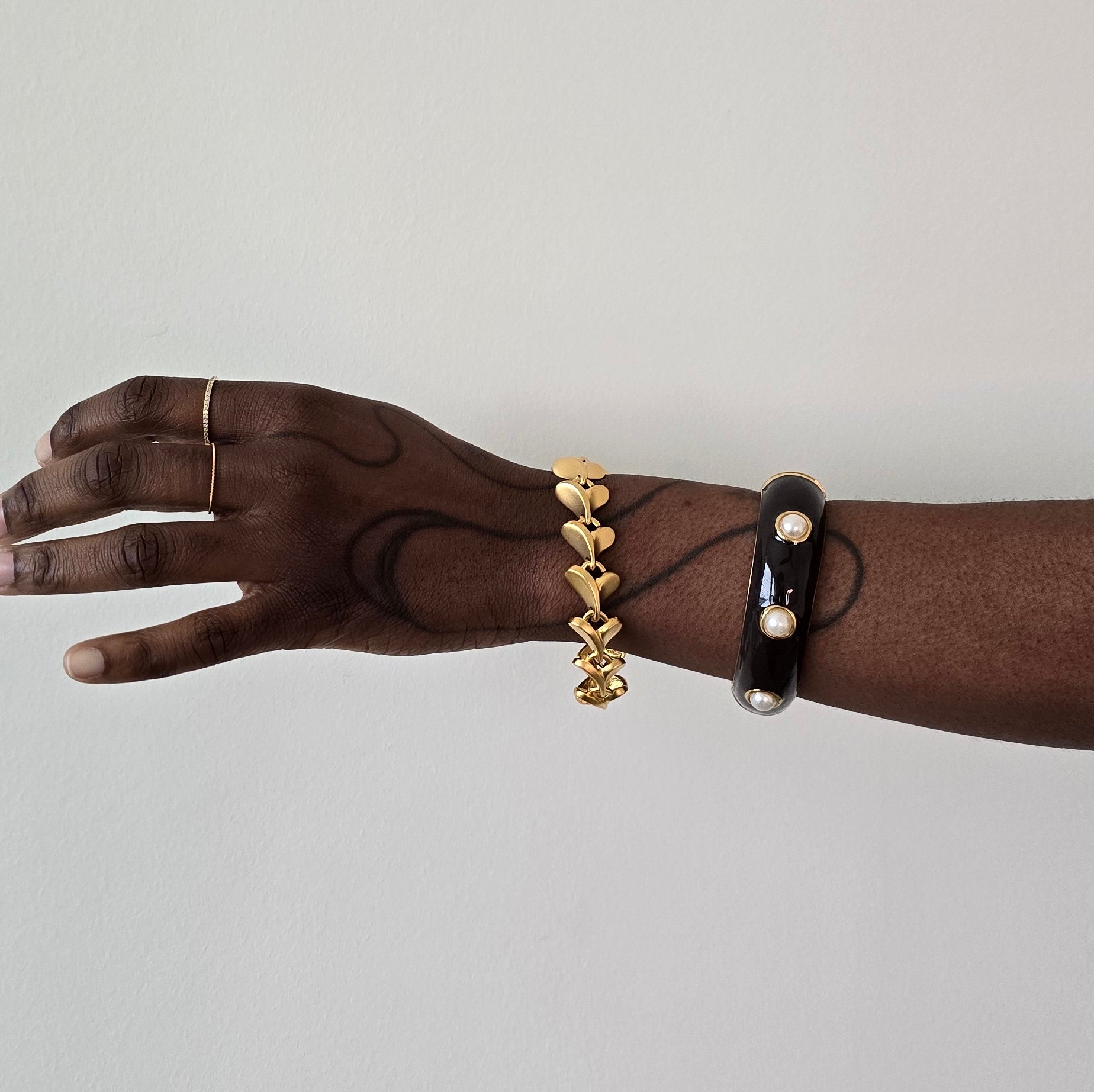 Hand wearing a gold bracelet and a black bracelet with pearls on a light gray background