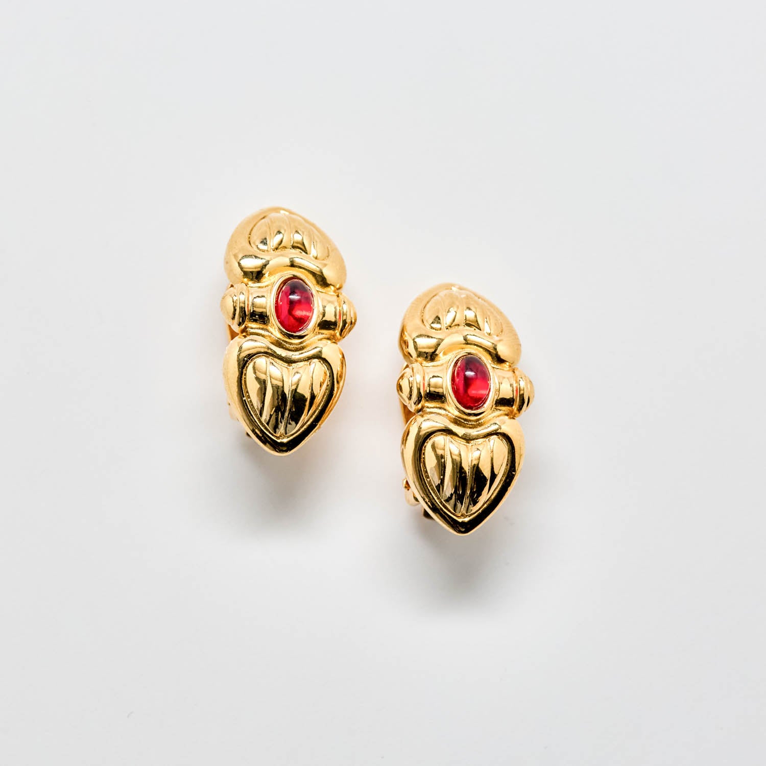 Gold heart-shaped earrings with red gemstones on a light gray background