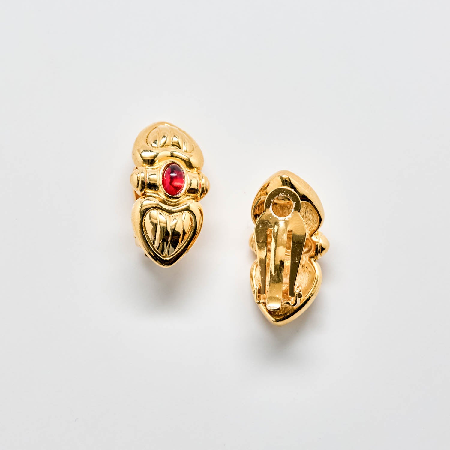 Gold earrings with a red gemstone on a light gray background