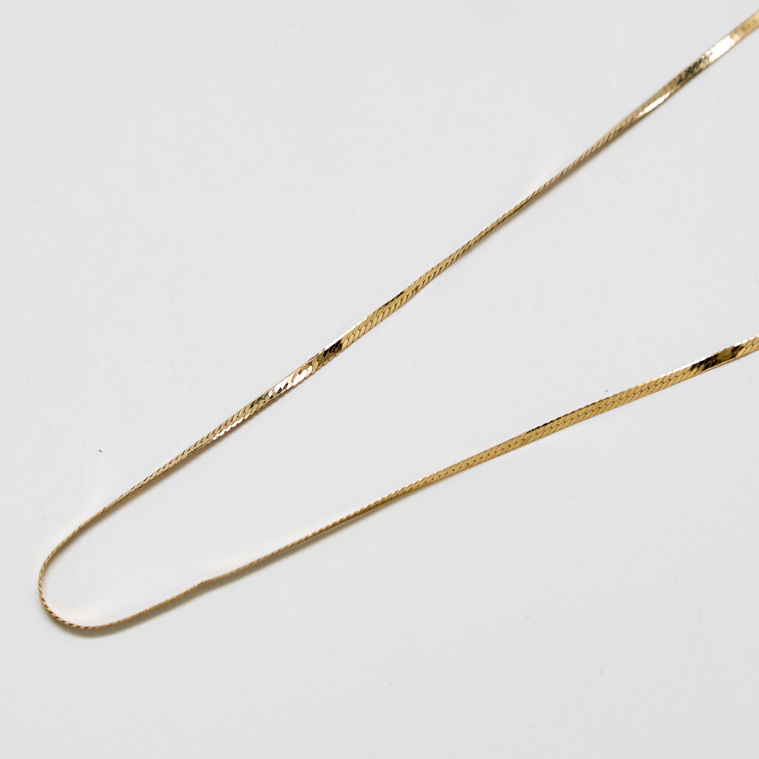 Close-up of vintage gold herringbone chain necklace showing flat, reflective links and polished finish.