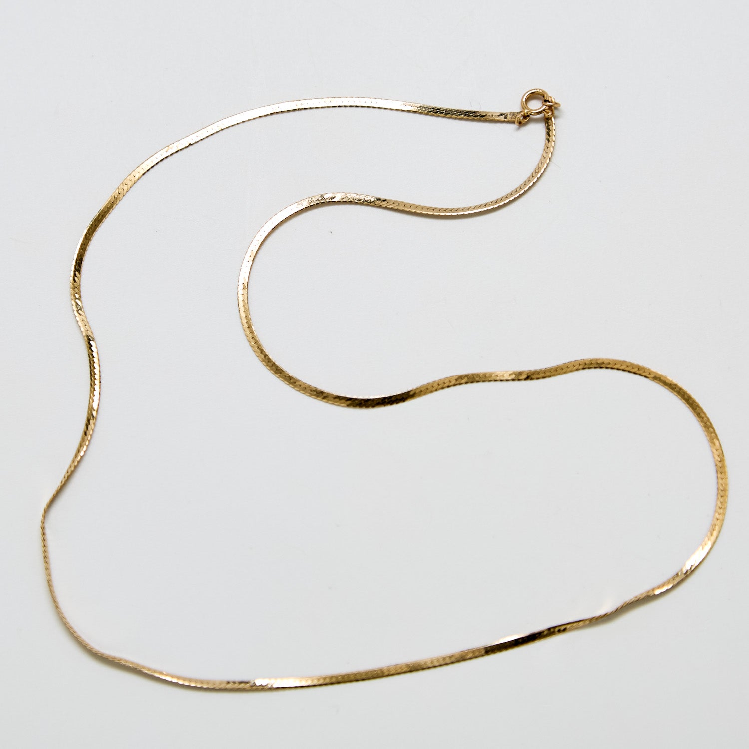 Full view of vintage gold-tone herringbone chain necklace laid in gentle curves with spring ring clasp