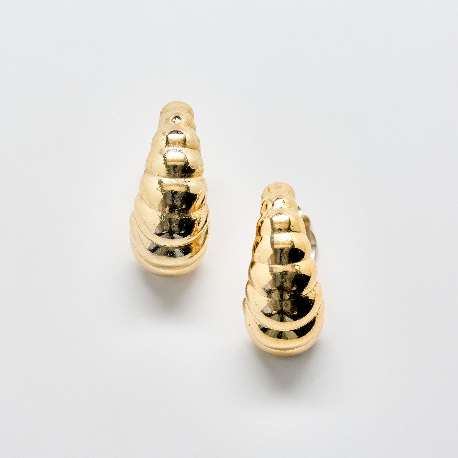 Pair of gold ribbed clip on earrings on a light gray background