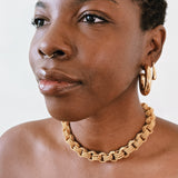 Woman wearing gold hoop earrings and a gold chain necklace against a white background