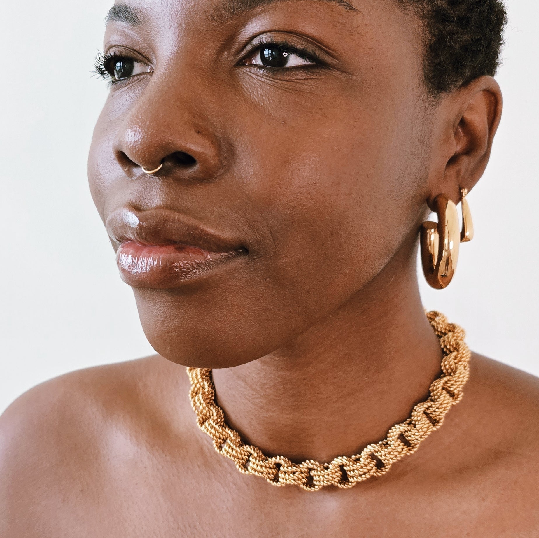 Woman wearing gold hoop earrings and a gold chain necklace against a white background