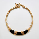 Gold and black necklace on a light gray background
