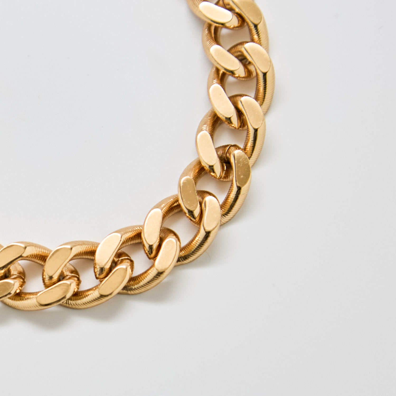 Close-up of vintage Monet gold chain bracelet showing polished curb links and textured edge detailing.