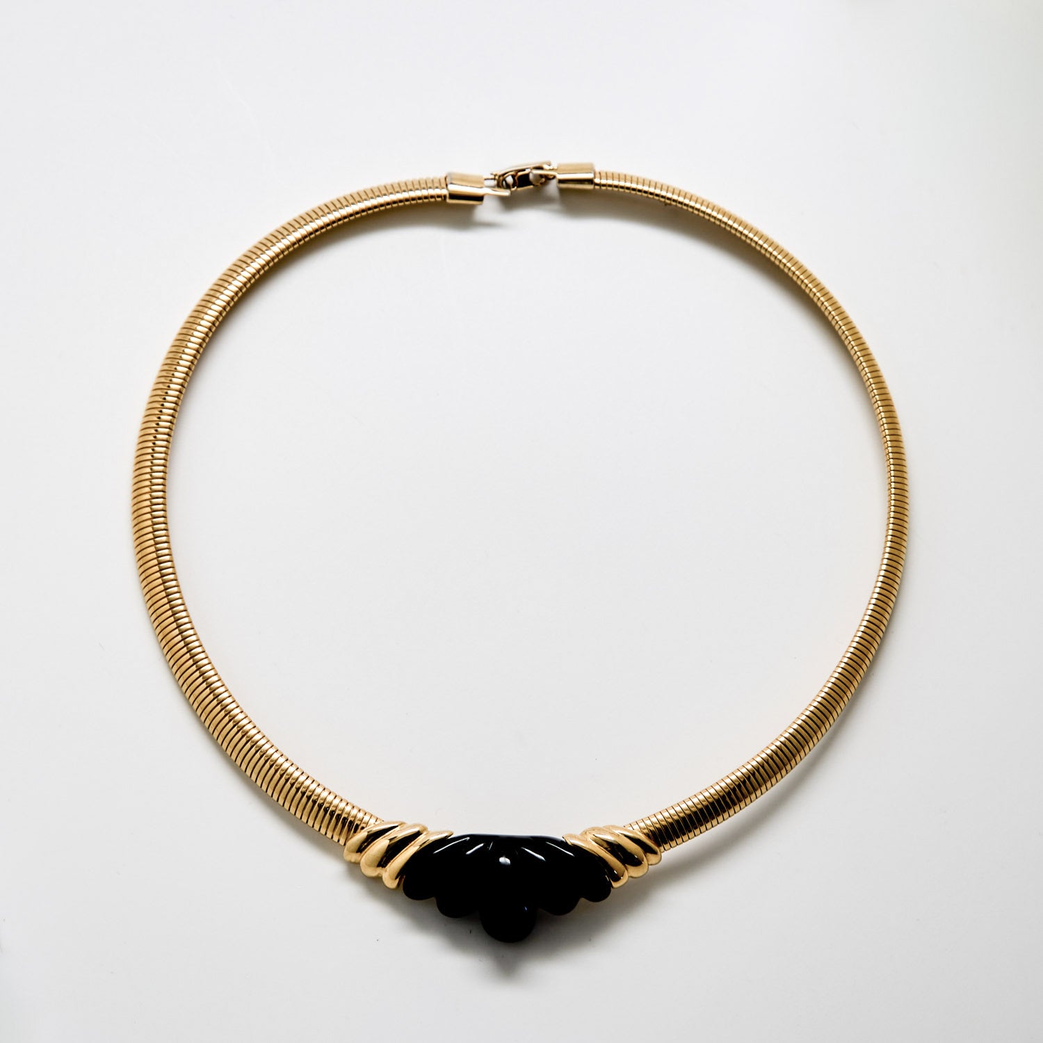 Gold necklace with a black pendant on a white background