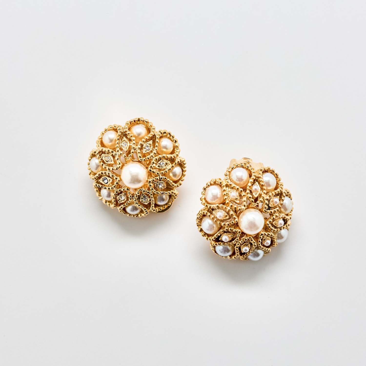 Gold earrings with pearl-like stones on a light gray background