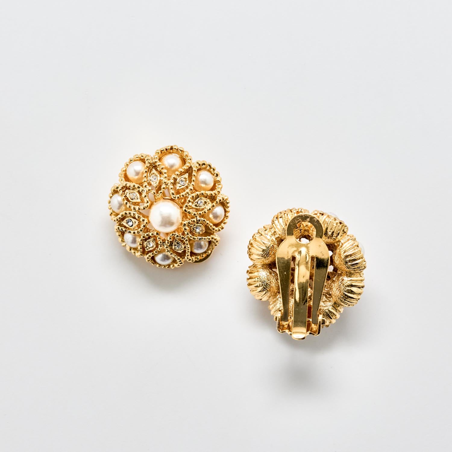 Gold earrings with pearl-like stones on a light gray background