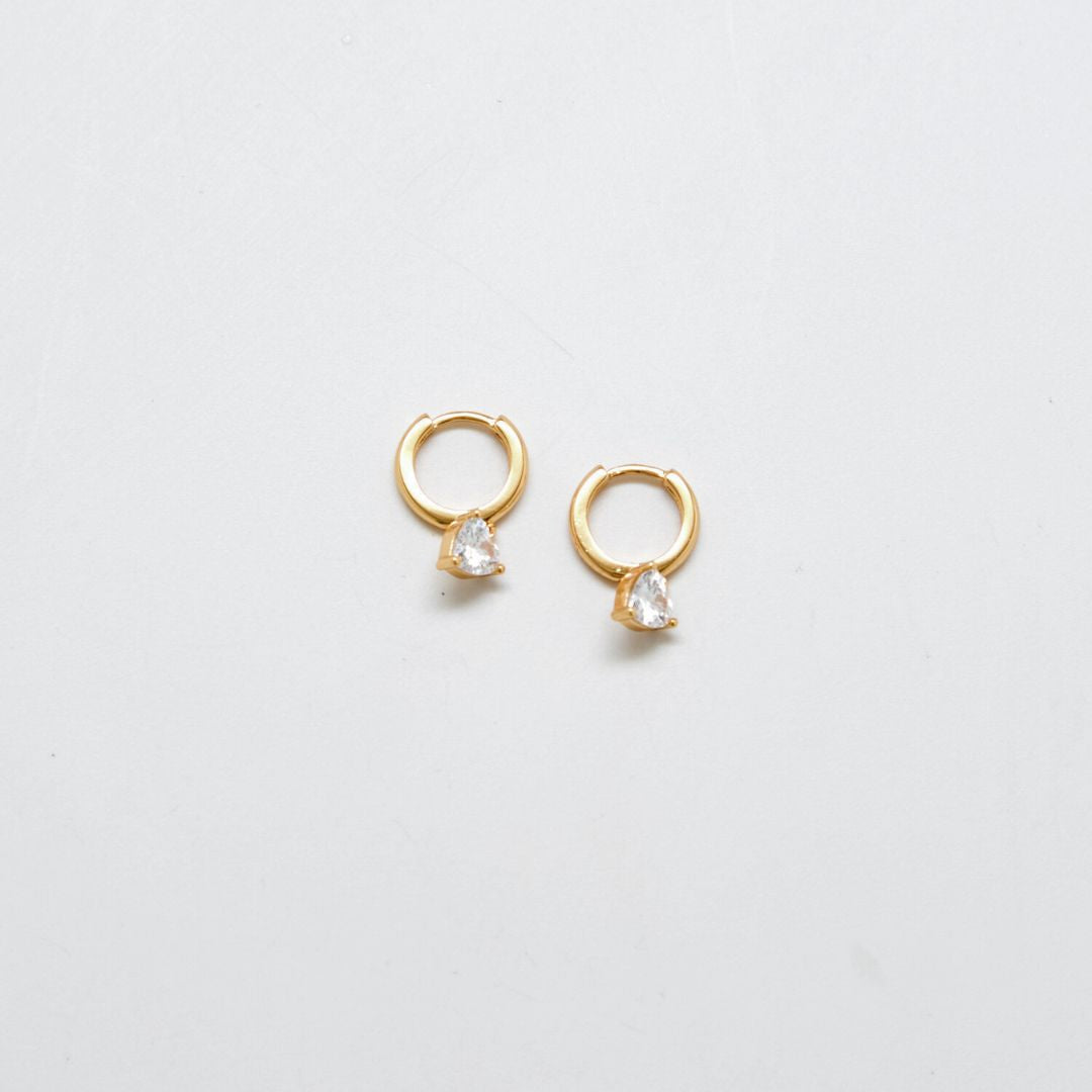 Gold CZ heart huggie earrings on white background.
