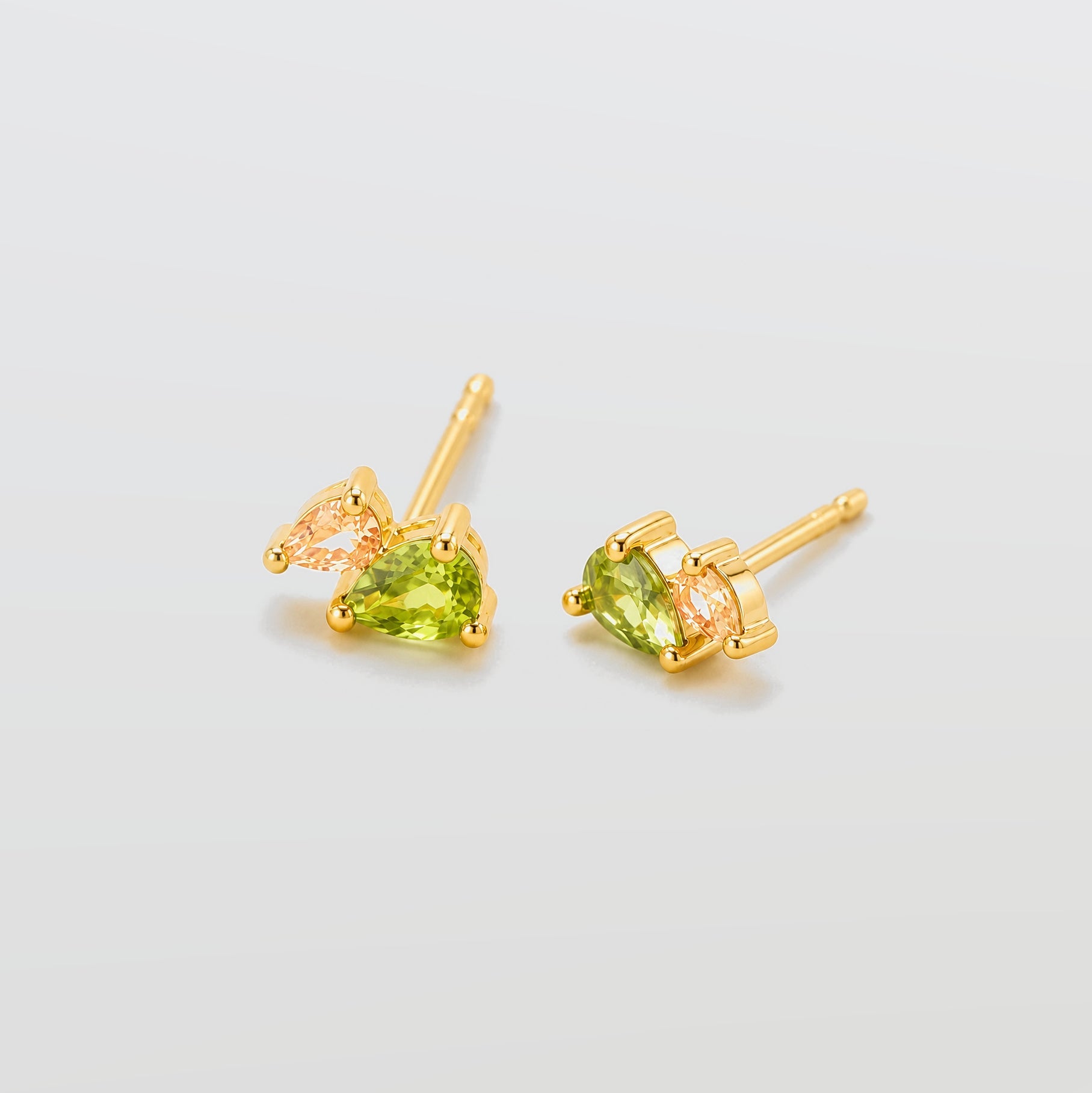 Gold earrings with green gemstones on a light gray background
