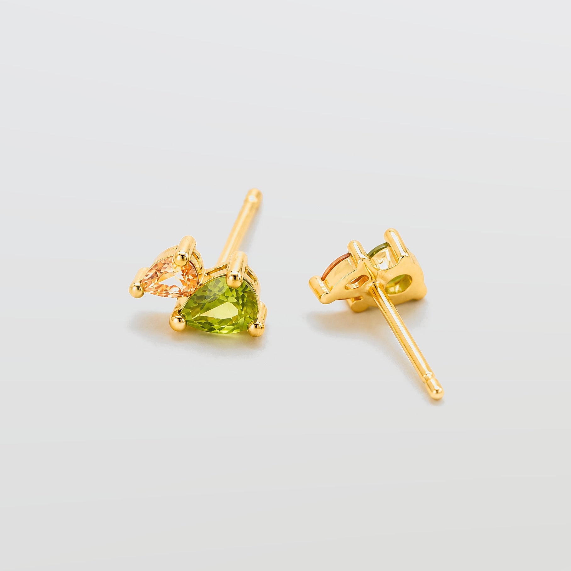 Gold earrings with green gemstones on a light gray background