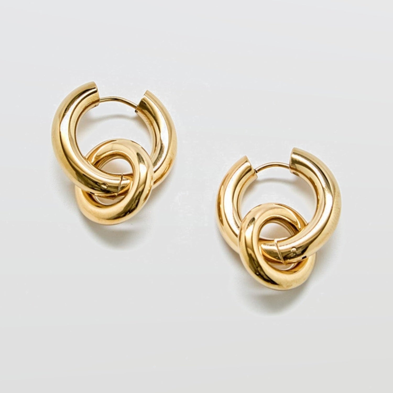 Gold interlocking hoop earrings against white background with removable charm detail in polished stainless steel, modern statement hoop design.