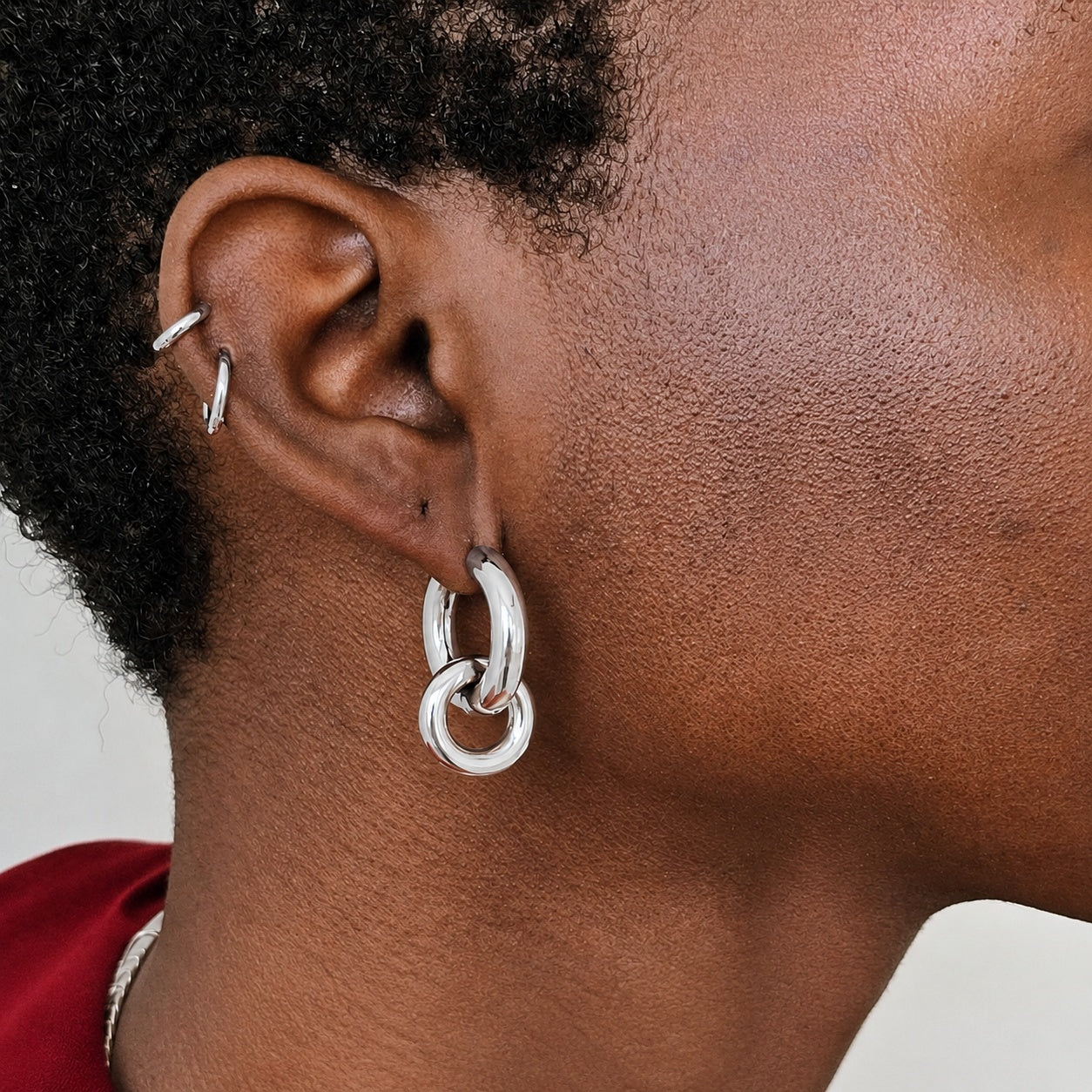 Close-up of an ear wearing silver hoop earrings with a neutral background