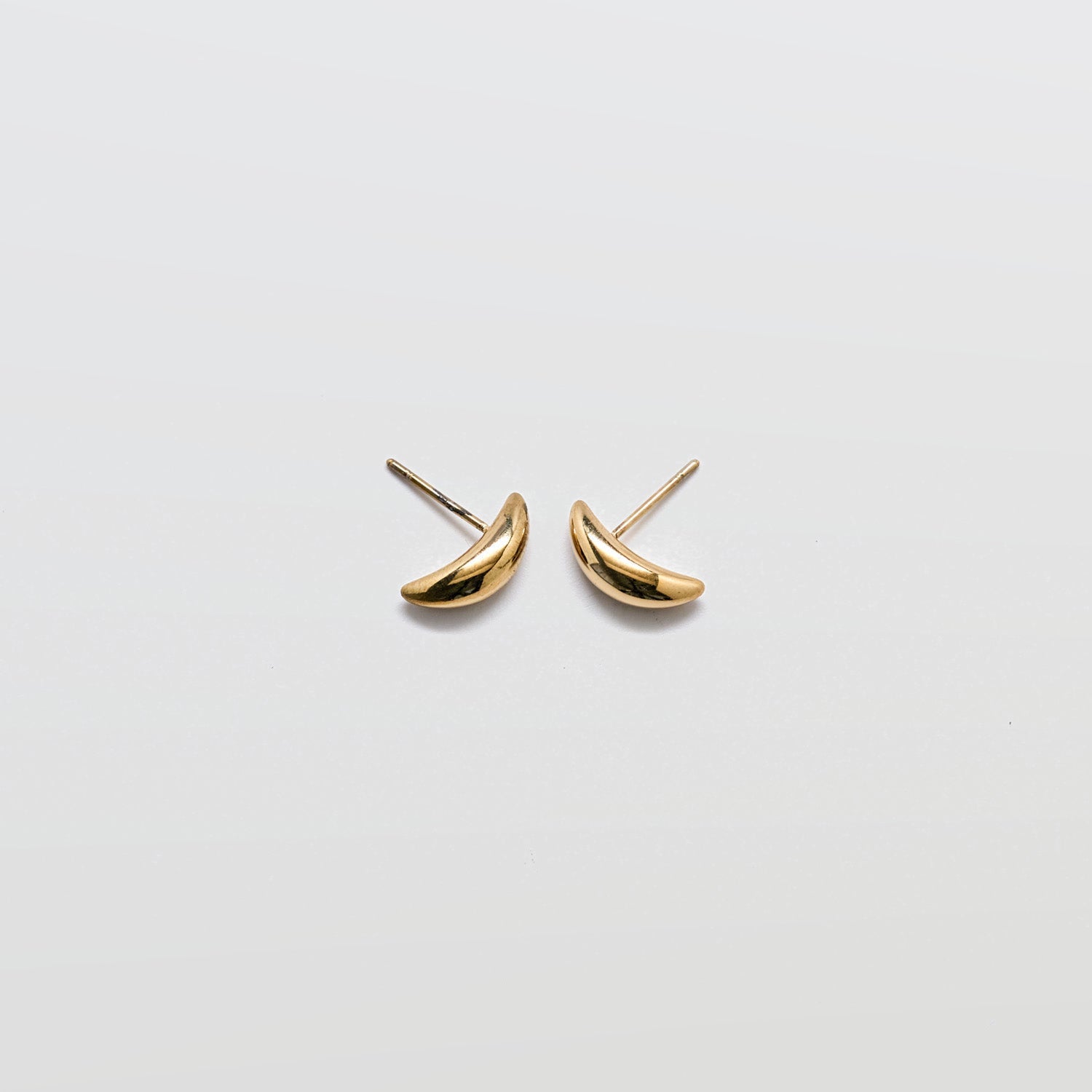 Pair of small curved gold stud earrings with a smooth polished finish and post backs against a white background
