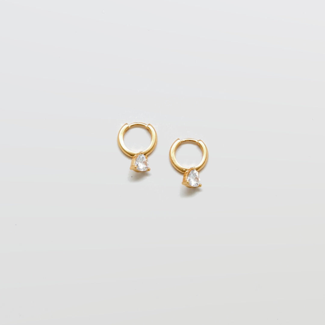 Gold CZ heart huggie earrings on white background.
