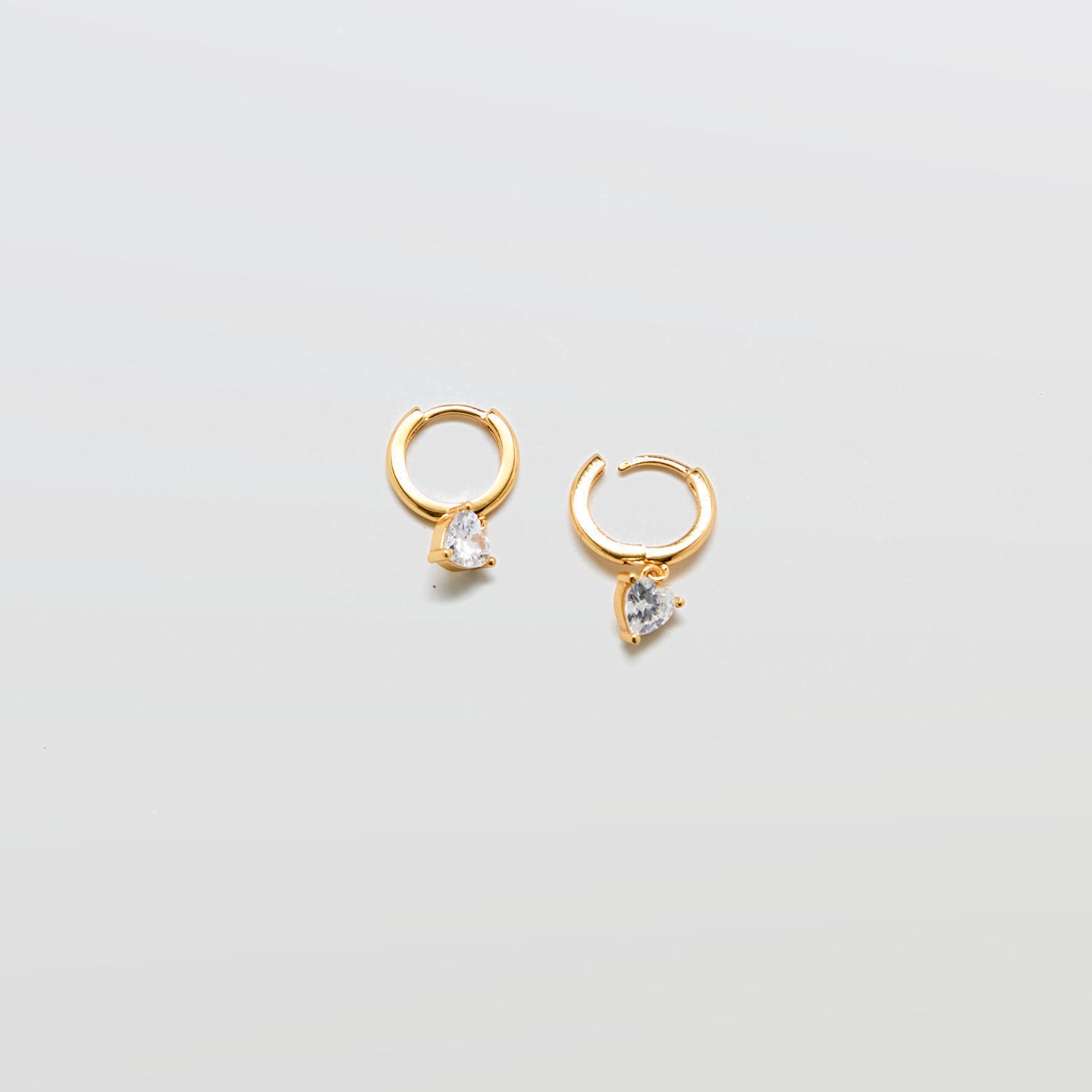 Gold huggie earrings with heart-shaped cubic zirconia accent and hinged hoop closure.
