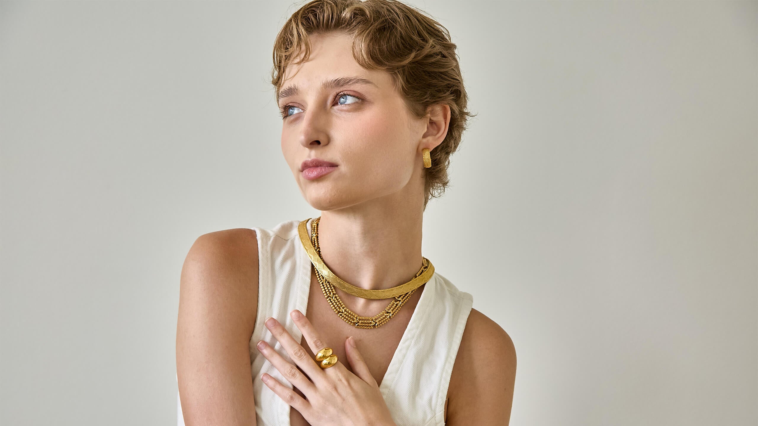Model wearing layered vintage gold necklaces and a gold ring