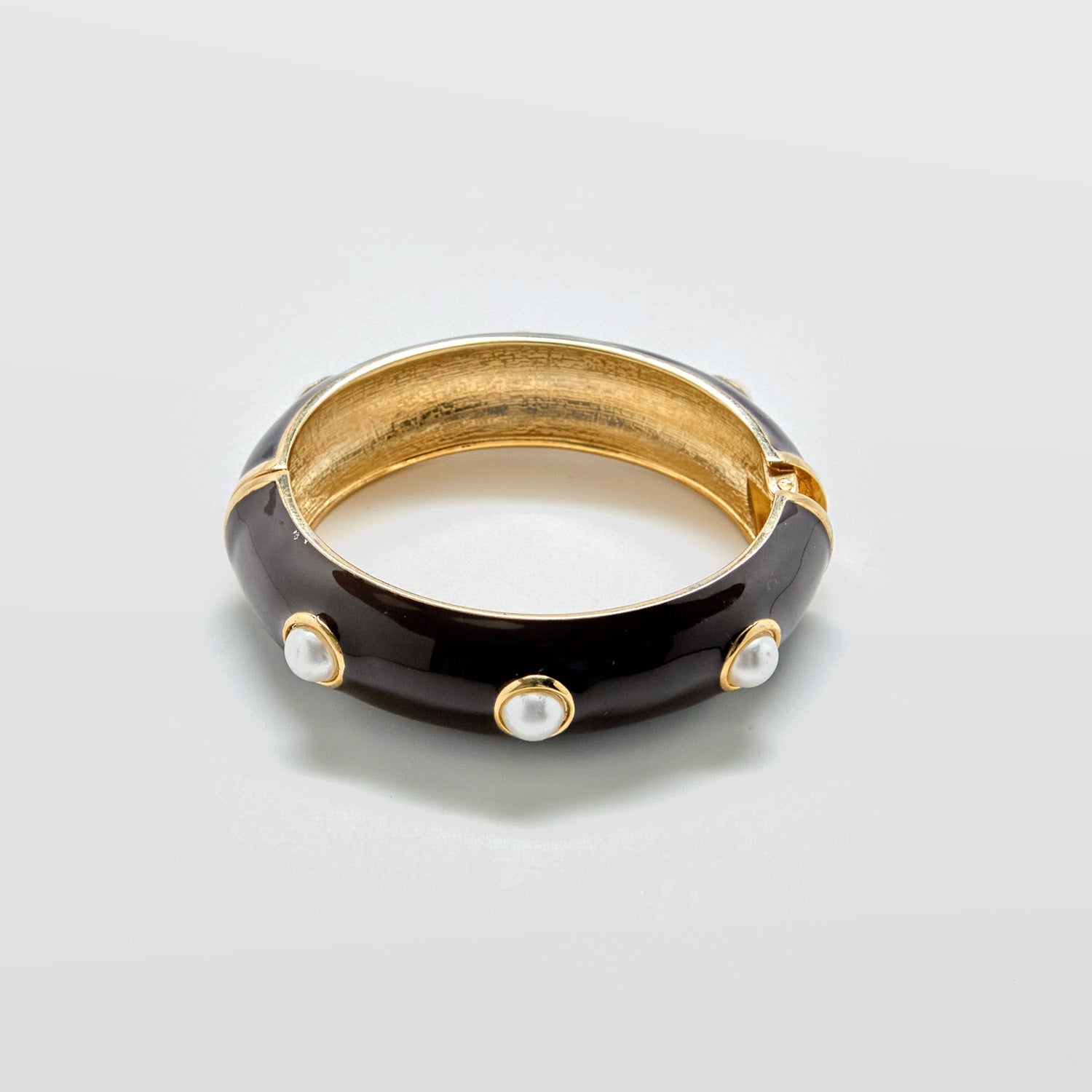 Black and gold bracelet with pearl-like stones on a light gray background