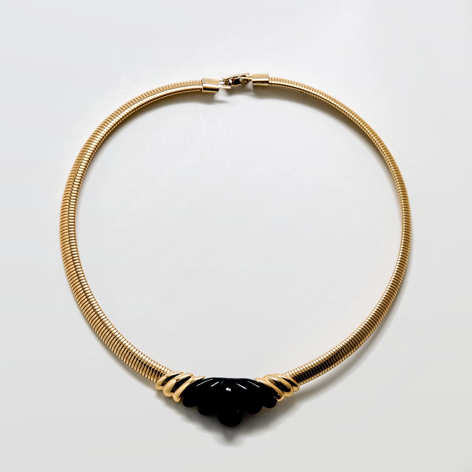 Gold necklace with a black pendant on a white background