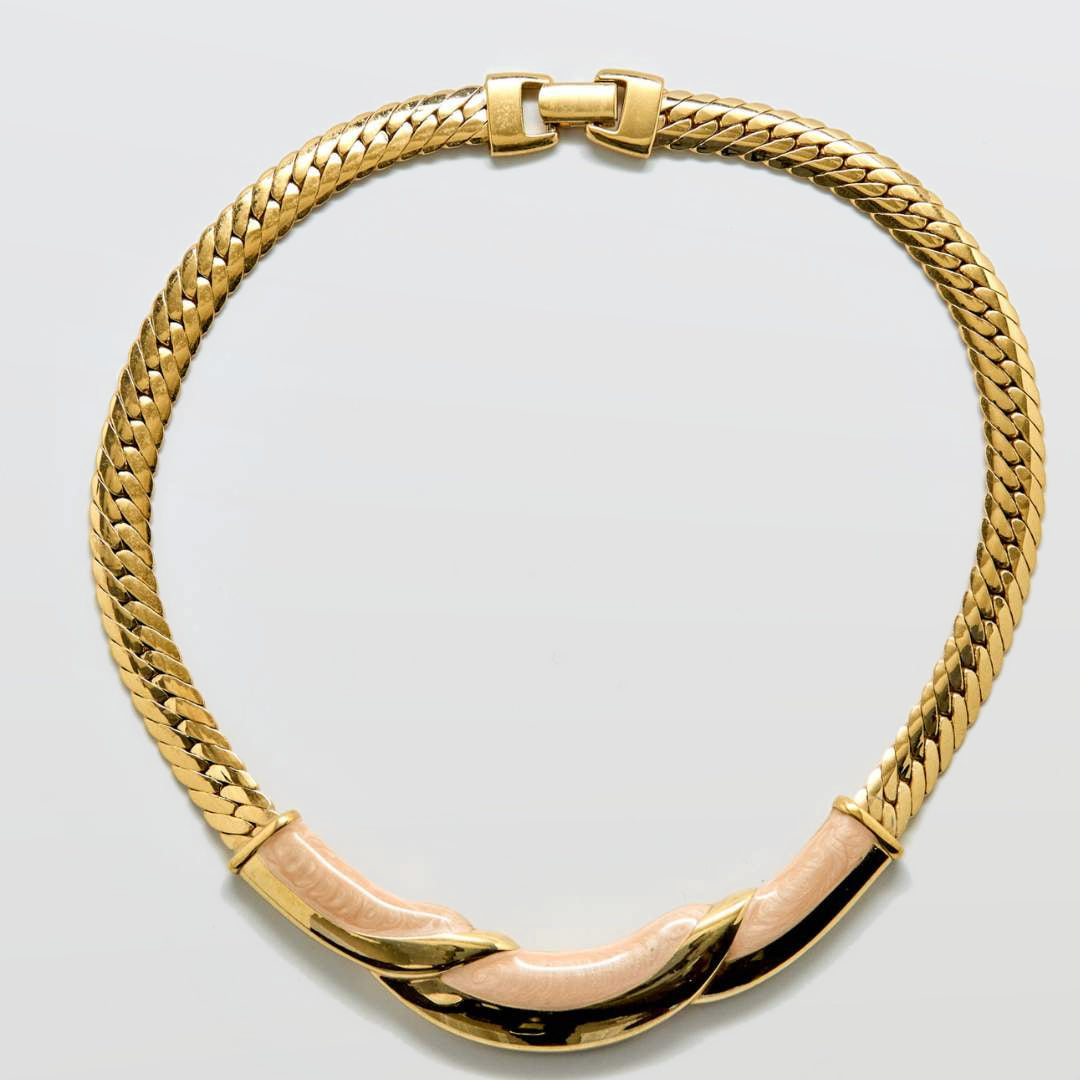 Gold chain necklace with a pink accent on a light gray background