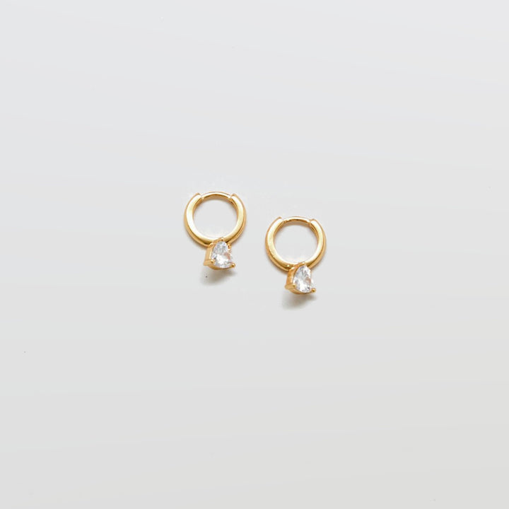 Gold CZ heart huggie earrings on white background.